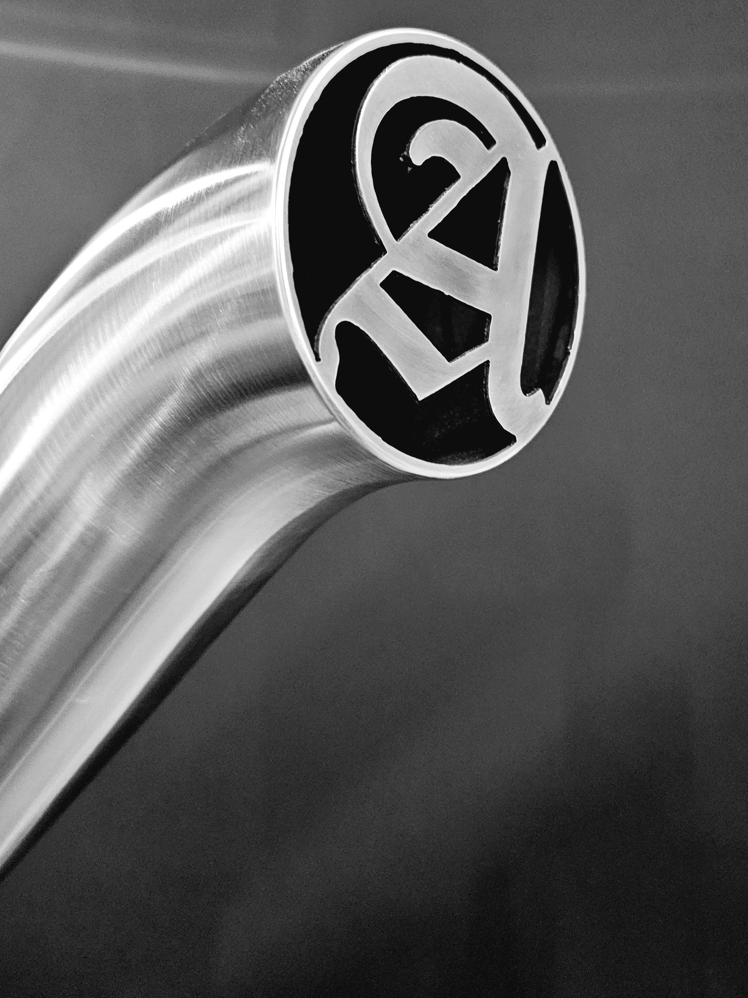 Close-up of a metallic, curved pipe with a stylized logo cutout at the end