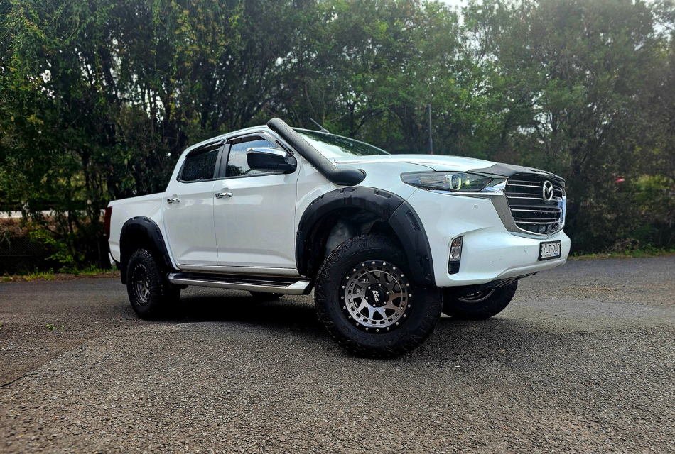 A white pickup truck with large tires and a snorkel is parked on a paved road.