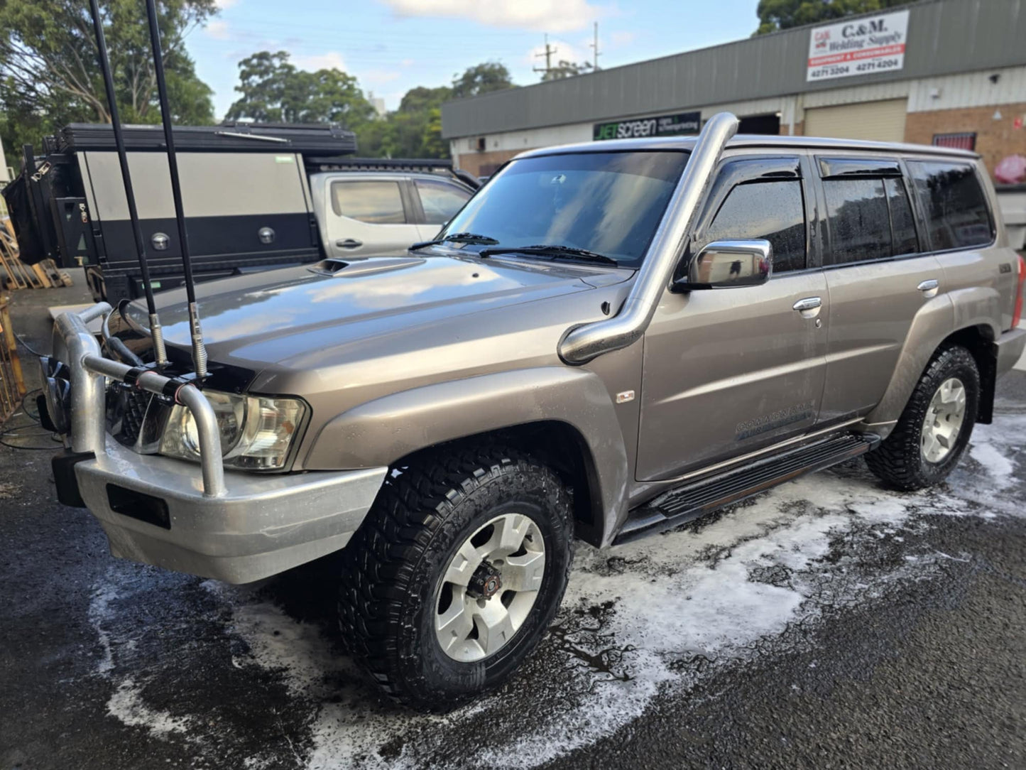 SUV in brown with off-road tires, snorkel, bull bar, parked on wet ground.
