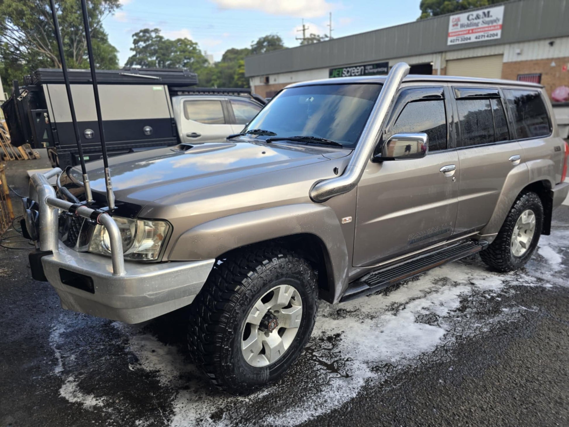A brown SUV with off-road tires, snorkel, and bull bar parked on a wet surface.
